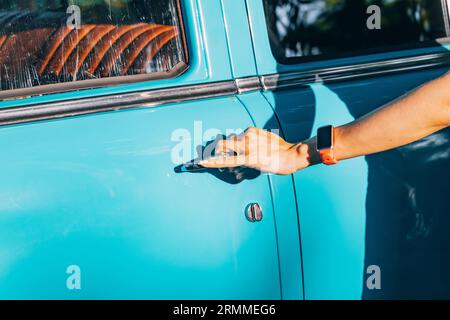 Facilità di guida estiva: La mano di una ragazza apre senza sforzo la porta di un'auto d'epoca retrò, mettendo in evidenza la comodità di viaggiare in auto e uno stile di vita spensierato. Foto Stock