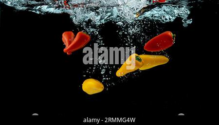 Peperoni dolci rossi e gialli, capsicum annuum, verdure che cadono in acqua su sfondo nero Foto Stock