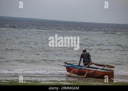 Pescatore solitario sulla spiaggia sabbiosa del Mozambico che prepara la barca per andare a vela e a pescare Foto Stock