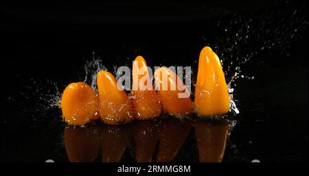 Peperoni dolci gialli, capsicum annuum, verdure che cadono sull'acqua su fondo nero, Foto Stock