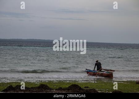 Pescatore solitario sulla spiaggia sabbiosa del Mozambico che prepara la barca per andare a vela e a pescare Foto Stock