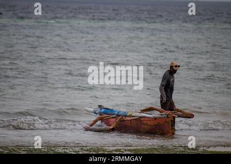 Pescatore solitario sulla spiaggia sabbiosa del Mozambico che prepara la barca per andare a vela e a pescare Foto Stock