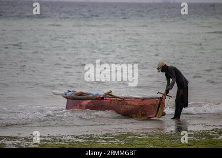 Pescatore solitario sulla spiaggia sabbiosa del Mozambico che prepara la barca per andare a vela e a pescare Foto Stock