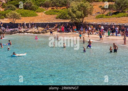 CRETA, GRECIA - 12 LUGLIO 2023: Folle di gente del posto e turisti su una piccola spiaggia rocciosa circondata da acque cristalline e turchesi su Kolokitha, Elounda, Creta Foto Stock