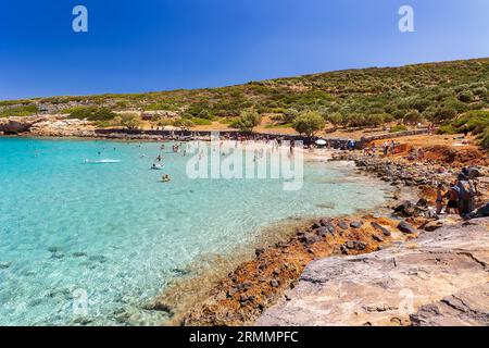 Folle di gente del posto e turisti su una piccola spiaggia rocciosa circondata da acque limpide e turchesi su Kolokitha, Elounda, Creta Foto Stock