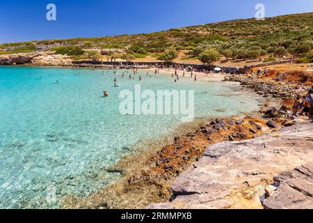 Folle di gente del posto e turisti su una piccola spiaggia rocciosa circondata da acque limpide e turchesi su Kolokitha, Elounda, Creta Foto Stock