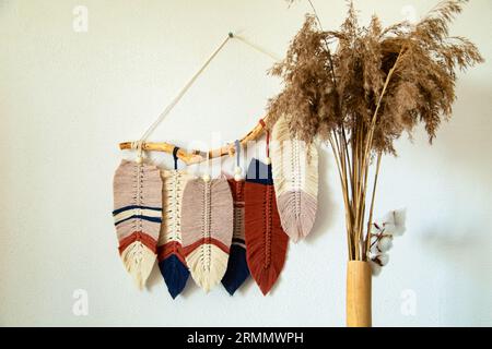 Pannello a parete in stile Boho realizzato con corde di cotone beige, blu e rosso utilizzando la tecnica del macrame. Arredamento moderno di tendenza, atmosfera intima, stile boho. Foto Stock