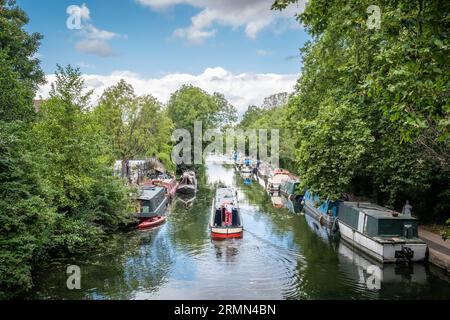Regent's Canal, Victoria Park, Hackney, Londra, Inghilterra - 29 luglio 2023: Una stretta barca passa tra le altre strette barche ormeggiate lungo il Regent's Canal Foto Stock