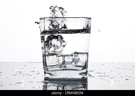 Acqua fredda in un bicchiere con cubetti di ghiaccio. Schizzi d'acqua. Rilassati in una calda giornata estiva. Immagine monocromatica. Foto Stock