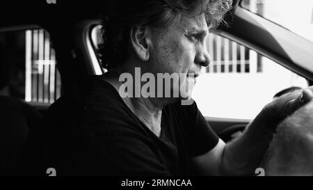 Senior Man che prova tristezza in auto parcheggiata, che tiene il volante, che lotta con la depressione, in bianco e nero Foto Stock