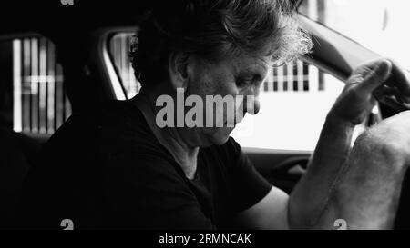 Senior Man che prova tristezza in auto parcheggiata, che tiene il volante, che lotta con la depressione, in bianco e nero Foto Stock