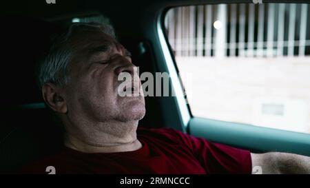 Uomo anziano che soffre di disperazione emotiva parcheggiato in auto, persona anziana che si appoggia al volante del veicolo in una quieta disperazione e disconnessione sociale Foto Stock