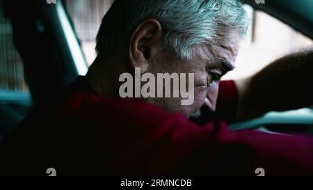 Uomo anziano che soffre di disperazione emotiva parcheggiato in auto, persona anziana che si appoggia al volante del veicolo in una quieta disperazione e disconnessione sociale Foto Stock