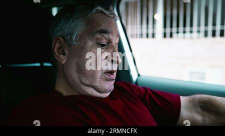 Uomo anziano che soffre di disperazione emotiva parcheggiato in auto, persona anziana che si appoggia al volante del veicolo in una quieta disperazione e disconnessione sociale Foto Stock