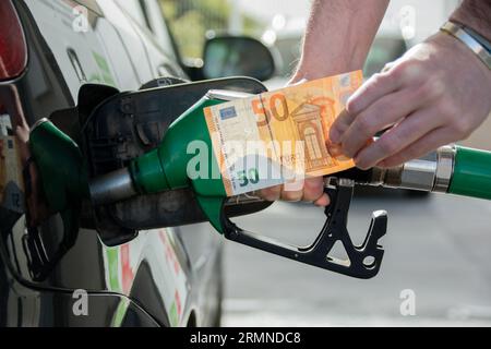 Le mani di un uomo che rifornisce la sua auto con una banconota da 50 euro. Concetto di aumento del costo della vita Foto Stock