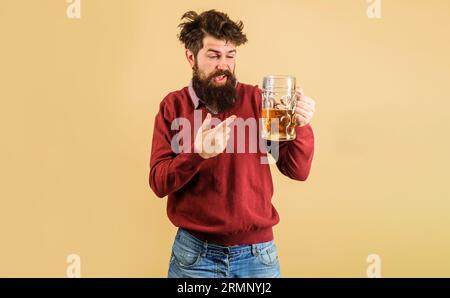 Un uomo ubriaco e barbuto che punta il dito contro la tazza di birra. Oktoberfest festival. Hipster barbuto con degustazione di birra fresca. Degustazione di birra. Bevete, alcol Foto Stock