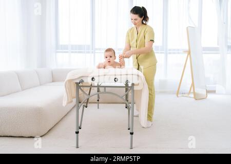 Ritratti di grandi dimensioni di massaggiatrice professionale che massaggia i piedi del neonato che accarezza delicatamente i piedi. Neonato piccolo che riceve riflessologia piedi a. Foto Stock