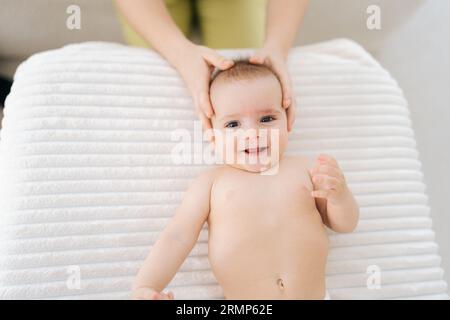 Vista dall'alto dell'allegro bambino manipolato da un terapista o un medico osteopatico manuale. Primo piano le mani della massaggiatrice femminile Foto Stock