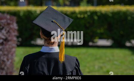 Una donna lancia il suo cappellino di laurea contro il cielo blu. Foto Stock