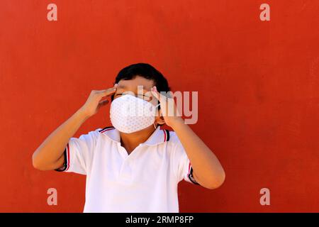 Felice e penoso Latino 8 anni ragazzo che indossa camicia bianca uniforme scolastica e maschera viso per la protezione nella pandemia di Covid-19 al ritorno a scuola Foto Stock