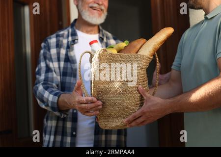 Uomo con un sacco di prodotti che aiuta il suo vicino più anziano all'aperto, primo piano Foto Stock