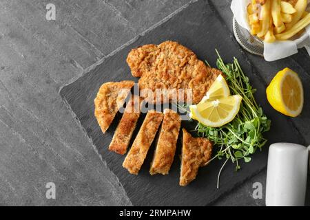 Gustosi schnitzels serviti con patatine fritte, microgreen e limone su tavola grigia, piatti Foto Stock