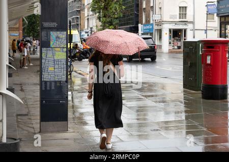 Una donna che cammina fuori sotto la pioggia e tiene un ombrello fuori dal Chelsea Hospital, Londra, Regno Unito Foto Stock