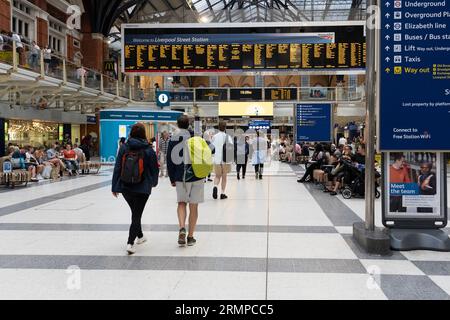 Passeggeri del treno che camminano attraverso la stazione ferroviaria di Liverpool Street con un cartello di benvenuto e orari di partenza del treno con bordo elettronico dietro. Londra, Inghilterra Foto Stock