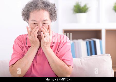 Frustrata e stressata nonna anziana che soffre di vista offuscata, dolore agli occhi affaticato. Foto Stock
