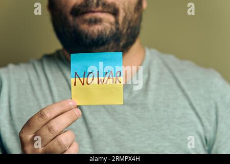 Un uomo europeo barbuto tiene davanti a sé un adesivo, sotto forma di bandiera Ucraina con l'iscrizione "no War" Foto Stock