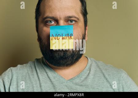 Un uomo europeo barbuto con un adesivo attaccato al naso, sotto forma di bandiera Ucraina con l'iscrizione "no War" Foto Stock