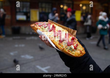 Mano che tiene il panino Zapiekanka a Cracovia, Polonia. Okrąglak Street food Court, Piazza ebraica Plac Nowy, Kazimierz, Kraków, Zapiekanki Krakowskie. Foto Stock