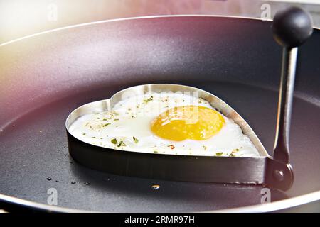 Preparare le uova fritte a forma di cuore per colazione Foto Stock