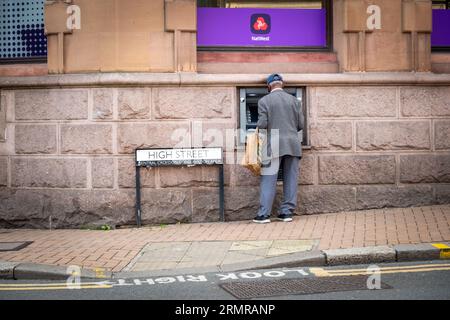 CROYDON, LONDRA - 29 AGOSTO 2023: Un anziano che ritira contanti da un bancomat NatWest a sud di Londra, vicino a un cartello di High Street Foto Stock