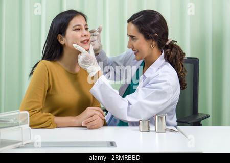 Closeup inspection by dermatologist examining facial skin condition of a young woman under clinical bright light Foto Stock