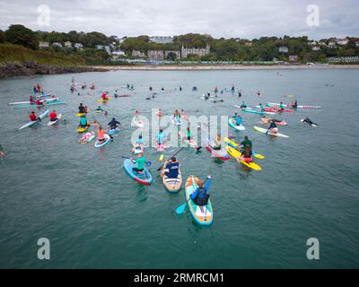 Il bagnino e la comunità di surf a Langland Bay, Swansea, hanno partecipato a una "pagaia" di massa dalla baia di Gower il lunedì sera, in memoria dell'uomo locale, Paul Carr. Paul è scomparso di recente all'età di 69 anni ed è stato un membro fondatore del Langland Bay Lifeguard Club e un membro molto amato della comunità. Oltre un centinaio di persone hanno rebbato o cimentato in Langland testa e hanno messo fiori sul mare in memoria di Paolo. Foto Stock