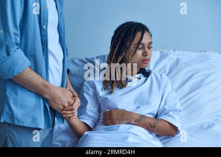 concetto di aborto spontaneo, uomo che tiene la mano della depressa moglie afroamericana, confortante, ospedale Foto Stock