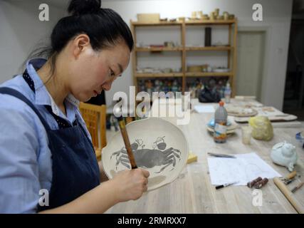 (140806) -- PECHINO, 6 agosto 2014 -- Zhang Lingyun lavora in uno studio nella sua casa a Jingdezhen, nella provincia del Jiangxi della Cina orientale, 18 luglio 2014. Zhang Lingyun ha 40 anni. Sono passati 20 anni da quando l'artista ceramico è venuto a Jingdezhen, capitale della porcellana cinese. La storia di Zhang con la ceramica ebbe un inizio casuale e romantico: Sapeva quasi nulla di ceramica prima di imbattersi nel nome Jingdezhen Ceramic Institute (JCI) quando si iscriveva al college. La ceramica sembrava interessante, quindi ho presentato la domanda per la JCI. Il capriccio d'impulso aveva fatto una grande differenza nella vita di Zhang. Il suo primo contatto wi Foto Stock