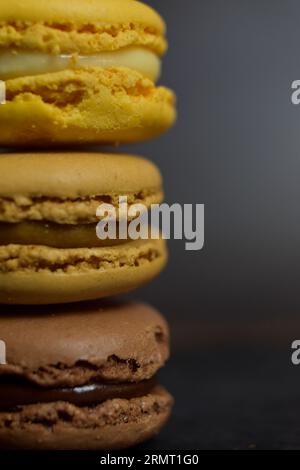 Macaron dai toni marrone e giallo impilati su sfondo nero, primo piano Foto Stock