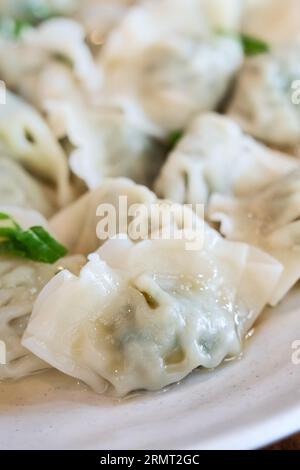Gnocchi di erba cipollina freschi e deliziosi con cipolle verdi, jiaozi in piatto bianco su fondo di legno. Foto Stock