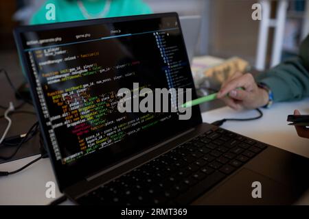 Concentratevi sullo schermo del notebook con dati codificati e penna tenuta per mano di un giovane insegnante o studente che presenta il nuovo software Foto Stock