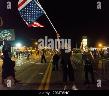 140819 -- FERGUSON, 19 agosto 2014 -- Un uomo sventola una bandiera nazionale degli Stati Uniti durante la protesta contro l'uccisione di Michael Brown da parte della polizia a Ferguson, Missouri, Stati Uniti, il 19 agosto 2014. Il 9 agosto, il diciottenne afro-americano Michael Brown è stato ucciso dalla polizia a Ferguson, scatenando una protesta della durata di una settimana nella città dove la maggior parte della popolazione è nera. Zhf US-MISSOURI-FERGUSON-PROTESTA ShenxTing PUBLICATIONxNOTxINxCHN Foto Stock