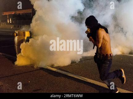 (140819) -- FERGUSON, 19 agosto 2014 -- Un manifestante corre dal fumo di bombole di gas lacrimogeni sparati dalla polizia durante le proteste contro l'uccisione di Michael Brown da parte della polizia a Ferguson, Missouri, Stati Uniti. Il diciottenne afro-americano Michael Brown fu ucciso dalla polizia a Ferguson, scatenando continue proteste nella città dove la maggior parte della popolazione è nera. ) US-MISSOURI-FERGUSON-PROTESTA-CLASH ShenxTing PUBLICATIONxNOTxINxCHN Ferguson 19 agosto 2014 un manifestante fuma di bombole SPARATE dalla polizia durante la protesta contro l'uccisione di Michael Brown a Ferguson Missouri Foto Stock