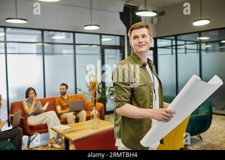 uomo d'affari felice con un progetto che guarda lontano vicino a colleghi sfocati che parlano in uno spazio di coworking Foto Stock