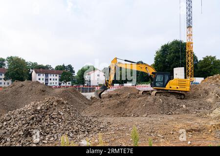 Un escavatore giallo in un cantiere di costruzione rastrella grandi cumuli di terra. Foto Stock