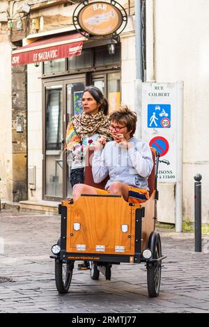 Madre e bambino parzialmente disabile in sella a una bici elettrica Eco-Triporteur assistita cargo - Tours, Indre-et-Loire (37), Francia. Foto Stock