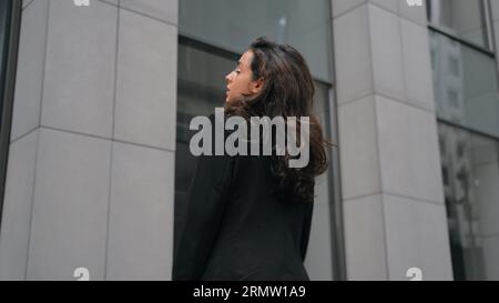 Donna caucasica con lunghi capelli scuri e vestito nero che si rivolge alla macchina fotografica, sorride e si mette le mani sul petto. Vista posteriore, primo piano, lento Foto Stock