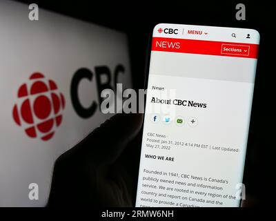 Persona che possiede uno smartphone con la pagina Web della Canadian Broadcasting Corporation (CBC) sullo schermo davanti al logo. Concentrarsi sul centro del display del telefono. Foto Stock