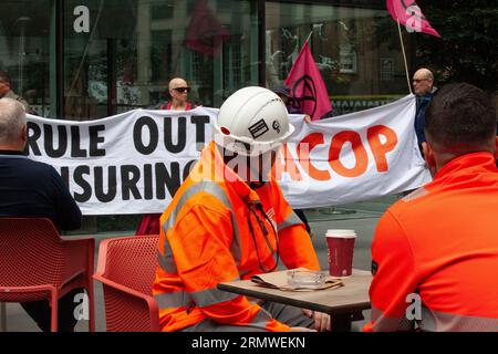 Londra, Regno Unito. 30 agosto 2023. I lavoratori che guardano al momento del loro unchbreak mentre i manifestanti di Extinction Rebellion prendono di mira 10 compagnie assicurative nella City di Londra, esortandoli a non assicurare il petrolio greggio dell'Africa orientale (EACOP). "Oil Slicker" in vernice bianca e nera marciava silenziosamente per le strade e all'esterno di ogni compagnia di assicurazioni l'olio simbolico (falso) è stato versato su un globo prima di essere pulito da una squadra in abiti hazmat. Crediti: Anna Watson/Alamy Live News Foto Stock