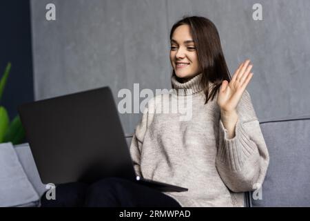 Giovane donna che ha una videochiamata via computer portatile in ufficio Foto Stock